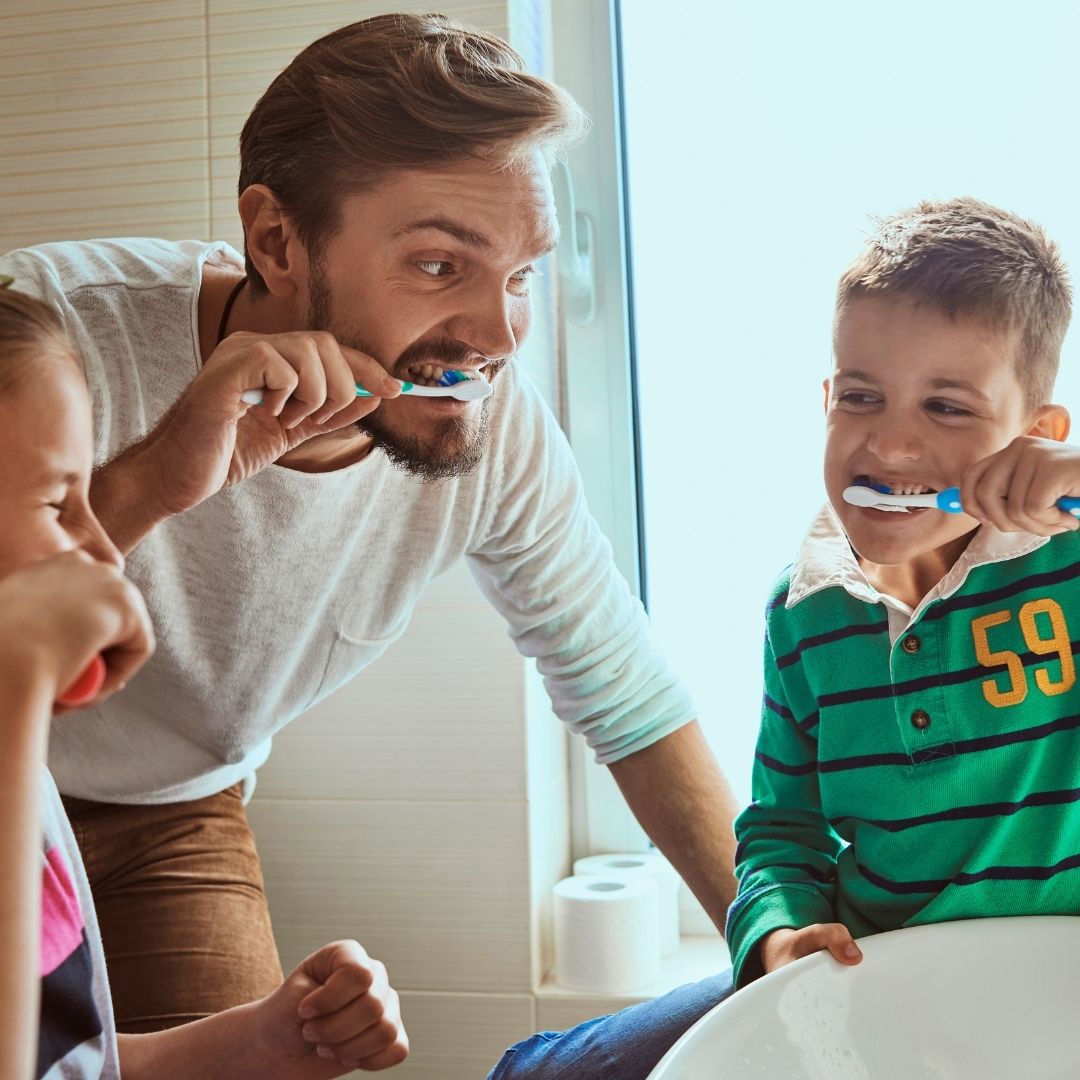 Dad brushing teeth with his kids.